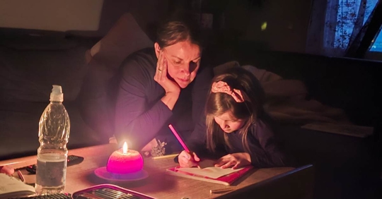 A mother watches her daughter draw during a power outage at home
