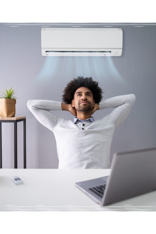 Comfortable man with hands behind his head in cool home office with cooling air unit behind him on the wall.